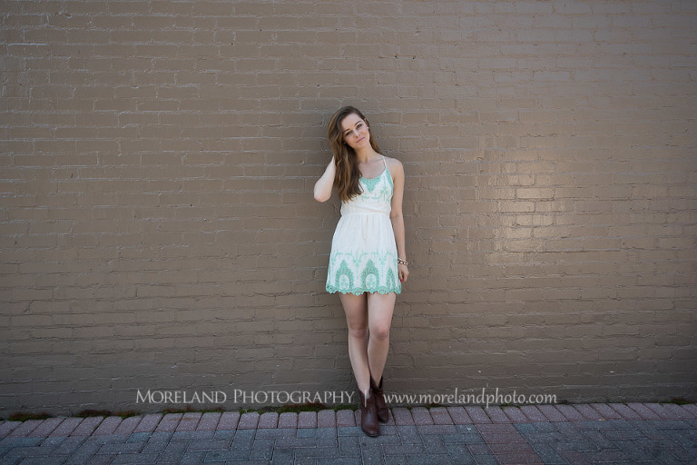 mikemoreland, morelandphoto, edgy, outdoors, long shot, soft lighting, big smile, white dress with blue design, boots, leaning against a wall