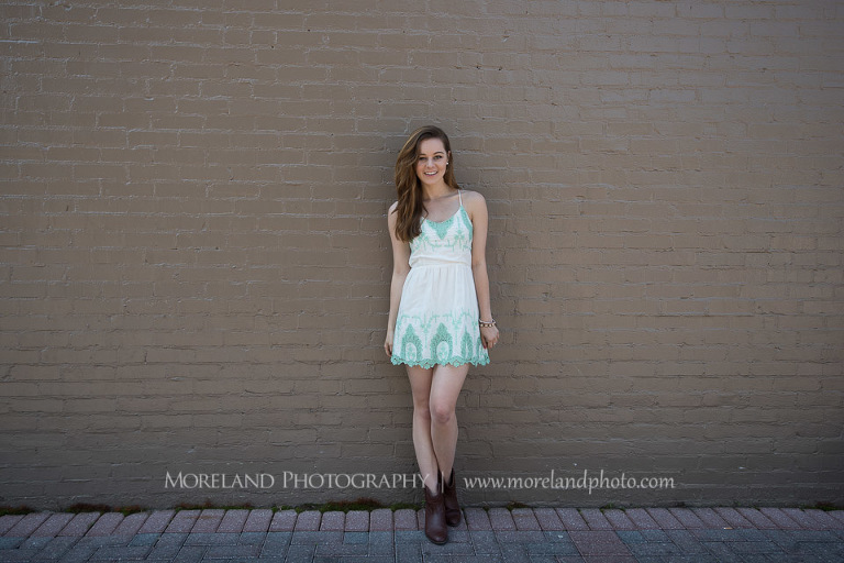 mikemoreland, morelandphoto, girly, fun, outdoors, long shot, soft lighting, big smile, white dress with blue design, boots, leaning on wall