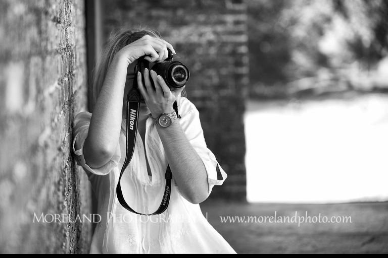 High school senior taking pictures with her camera as she leans against a brick wall, Roswell Senior Photography, Atlanta Senior Portraits, Senior Photography, Atlanta Senior Photography, Moreland Photography, Mike Moreland, Class of 2016, mikemoreland, morelandphoto, excitement, class of 2016, country girl, sparkling future, big grin, posing by wall, white blouse, medium shot portrait, photographer in action