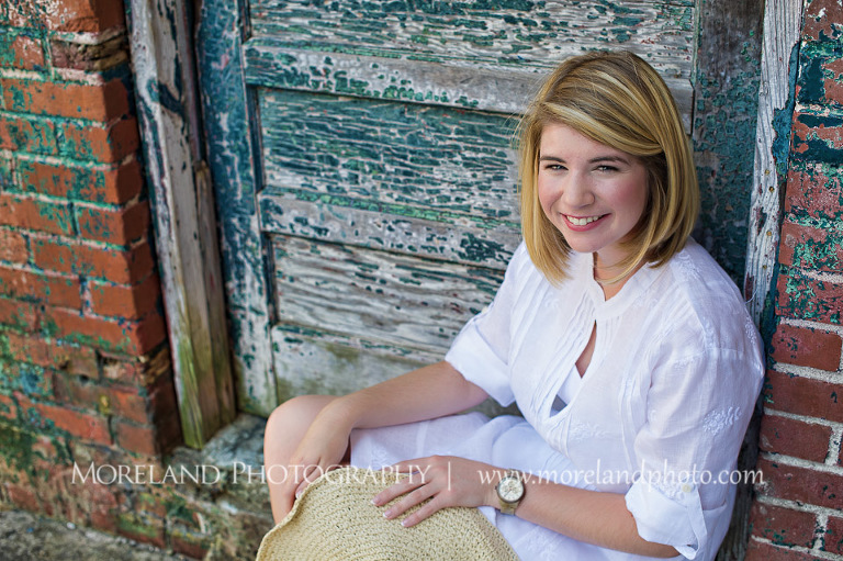 High school senior sitting by an old door with a hat in her hand, Roswell Senior Photography, Atlanta Senior Portraits, Senior Photography, Atlanta Senior Photography, Moreland Photography, Mike Moreland, Class of 2016, mikemoreland, morelandphoto, excitement, class of 2016, country girl, sparkling future, big grin, posing by door, white blouse, sitting portrait