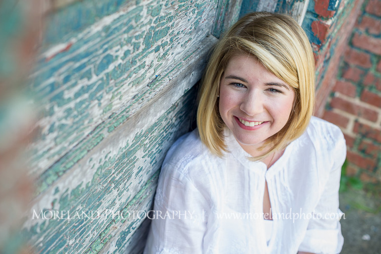 High school senior smiling as she is sitting by an old door, Roswell Senior Photography, Atlanta Senior Portraits, Senior Photography, Atlanta Senior Photography, Moreland Photography, Mike Moreland, Class of 2016, mike moreland, morelandphoto, excitement, class of 2016, country girl, sparkling future, big grin, posing by door, white blouse, sitting portrait, medium-close up