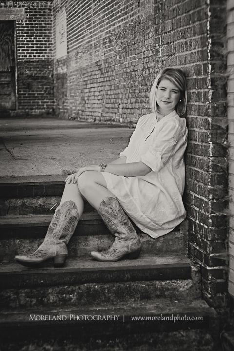 High school senior sitting on the steps with her back to the brick wall, Roswell Senior Photography, Atlanta Senior Portraits, Senior Photography, Atlanta Senior Photography, Moreland Photography, Mike Moreland, Class of 2016, mikemoreland, morelandphoto, relaxed, class of 2016, country girl, sparkling future, big grin, posing by door, white blouse, sitting portrait, long shot black and white photography, cowgirl boots, 