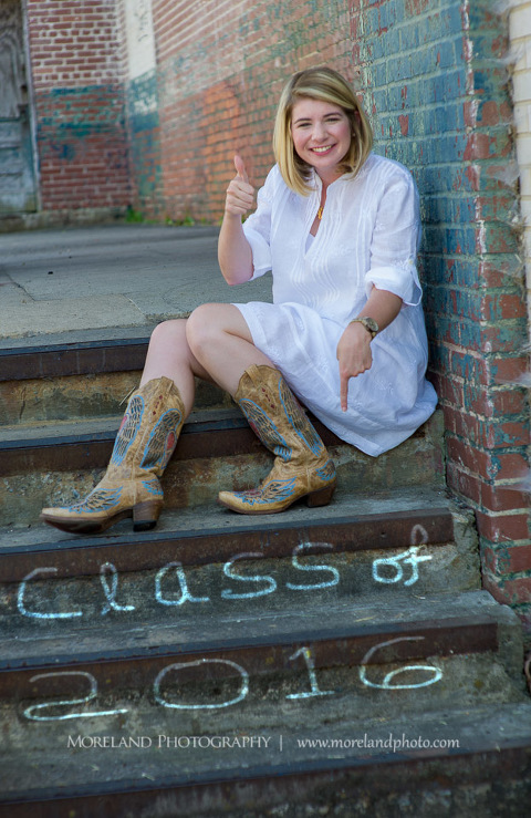 High school senior sitting on the steps with her back to the brick wall and she is pointing to the words class of 2016 and she is giving a thumbs up, Roswell Senior Photography, Atlanta Senior Portraits, Senior Photography, Atlanta Senior Photography, Moreland Photography, Mike Moreland, Class of 2016, mikemoreland, morelandphoto, excitement, class of 2016, country girl, sparkling future, big grin, posing by stairs, white blouse, sitting portrait