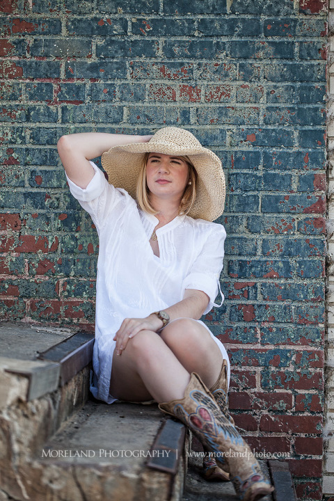 High school senior sitting on steps her back to the brick wall and her hand keeping her hat on her head, Roswell Senior Photography, Atlanta Senior Portraits, Senior Photography, Atlanta Senior Photography, Moreland Photography, Mike Moreland, Class of 2016, mikemoreland, morelandphoto, excitement, class of 2016, country girl, sparkling future, big grin, posing by stairs, white blouse, sitting portrait, eloquent and classy, strawhat, cowgirl boots