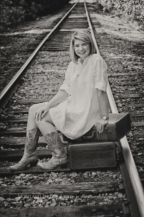 High school senior sitting on two suitcases on abandoned railroad tracks, Roswell Senior Photography, Atlanta Senior Portraits, Senior Photography, Atlanta Senior Photography, Moreland Photography, Mike Moreland, Class of 2016, mikemoreland, morelandphoto, excitement, class of 2016, country girl, sparkling future, big grin, posing by train tracks, white blouse, model portrait, afternoon, cowgirl boots, black and white photography, suitcase posing