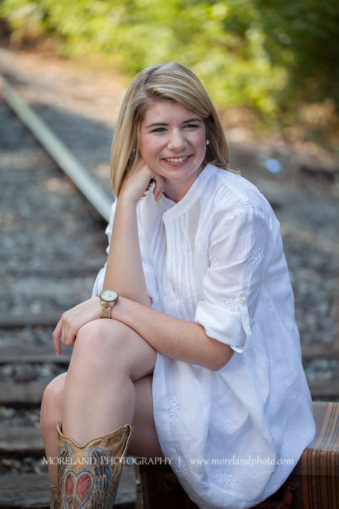 High school senior sitting on two suitcases on abandoned railroad tracks, Roswell Senior Photography, Atlanta Senior Portraits, Senior Photography, Atlanta Senior Photography, Moreland Photography, Mike Moreland, Class of 2016, mikemoreland, morelandphoto, excitement, class of 2016, country girl, sparkling future, big grin, posing by train tracks, white blouse, model portrait, afternoon, cowgirl boots, medium shot portrait