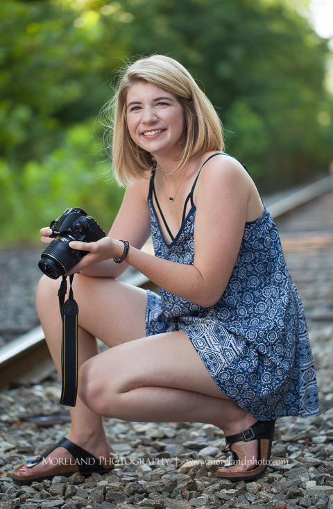 High school senior crouching down and holding her camera on abandoned railroad tracks, Roswell Senior Photography, Atlanta Senior Portraits, Senior Photography, Atlanta Senior Photography, Moreland Photography, Mike Moreland, Class of 2016, mikemoreland, morelandphoto, excitement, class of 2016, country girl, sparkling future, big grin, posing by train tracks, mixed color blouse, model portrait, afternoon, black and white photography, having fun, playing on the railroad, taking photos