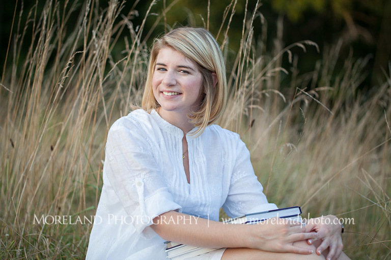 High school senior sitting in a tall grass field with books in her lap, Roswell Senior Photography, Atlanta Senior Portraits, Senior Photography, Atlanta Senior Photography, Moreland Photography, Mike Moreland, Class of 2016, mikemoreland, morelandphoto, excitement, class of 2016, country girl, sparkling future, big grin, classy and sassy, model portrait, white blouse, afternoon, yearbook editor, having fun, sitting in the field, bookworm 