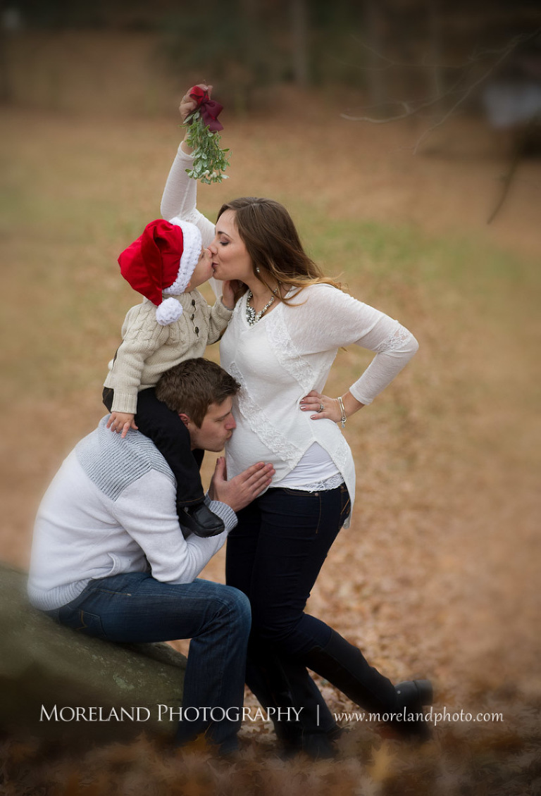 A Christmas themed pose with the pregnant wife kissing her son under the mistletoe while he is on his father's shoulders while the father is kissing his wife's stomach, hollywood maternity, beautiful, serene, love, joy, happiness, classic, timeless