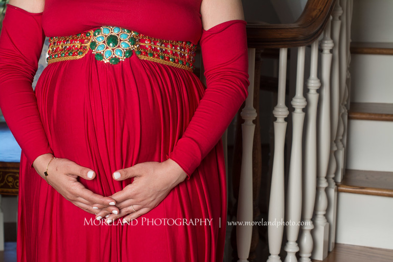 Close up of mother in elegant red maternity dress holding pregnant belly standing next to staircase, pregnancy, sophisticated pregnancy photo shoot, red maternity dress, Atlanta area photography, Atlanta area maternity photographers, fashion maternity shoots, regal estates for photos, mike moreland photography