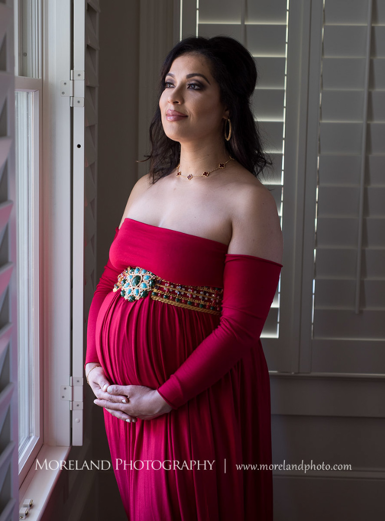 Regal pregnant woman in gorgeous red dress cradling pregnant belly gazing out of a window with a faint smile, pregnancy, romantic pregnancy photo shoot, red maternity dress, Atlanta area photography, Atlanta area maternity photographers, fashion maternity shoots, regal estates for photos, mike moreland photography 