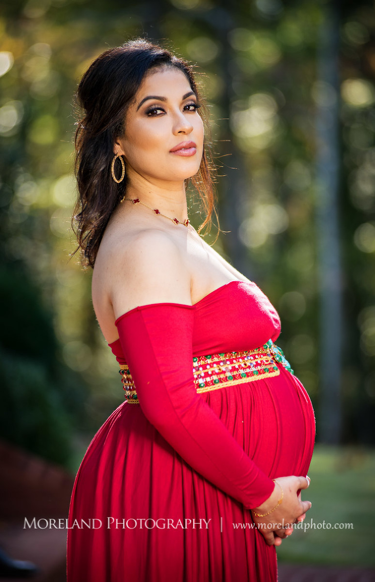 Side view of elegant pregnant woman in sophisticated red maternity dress looking at camera while cradling belly outside, pregnancy, romantic pregnancy photo shoot, outdoor maternity photo shoot, red maternity dress, Atlanta area photography, Atlanta area maternity photographers, fashion maternity shoots, regal estates for photos, mike moreland photography 