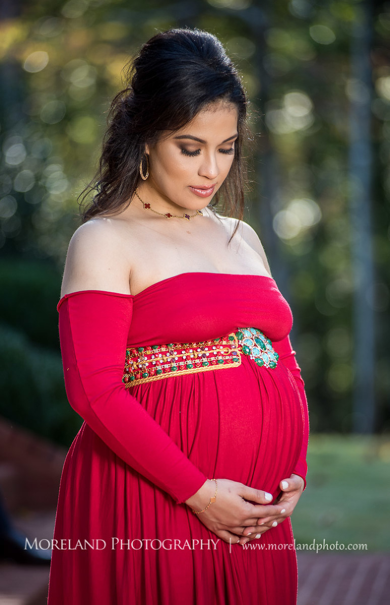 Elegant pregnant woman in sophisticated red maternity dress with eyes closed looking down while cradling belly outside, pregnancy, romantic pregnancy photo shoot, outdoor maternity photo shoot, red maternity dress, Atlanta area photography, Atlanta area maternity photographers, fashion maternity shoots, regal estates for photos, mike moreland photography 