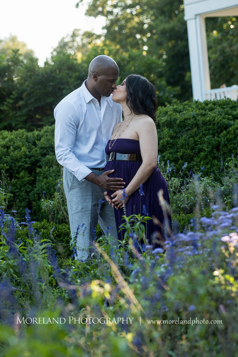Interracial couple kissing in the middle of a garden while cradling wife's pregnant belly, pregnancy, interracial couple, romantic pregnancy photo shoot, purple maternity dress, outdoor maternity photo shoot, romantic moment, romantic photo shoot, Atlanta area photography, Atlanta area maternity photographers, fashion maternity shoots, regal estates for photos, mike moreland photography 
