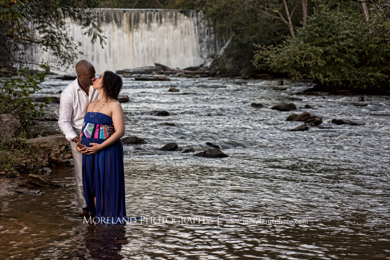 Interracial couple kissing in the middle of a river with a waterfall behind them, pregnancy, interracial couple, outdoor pregnancy photo shoots, maternity shoots with nature, fun maternity shoots, romantic pregnancy photo shoot, purple maternity dress, outdoor maternity photo shoot, romantic moment, romantic photo shoot, maternity photo shoots with water, Atlanta area photography, Atlanta area maternity photographers, fashion maternity shoots, mike moreland photography 