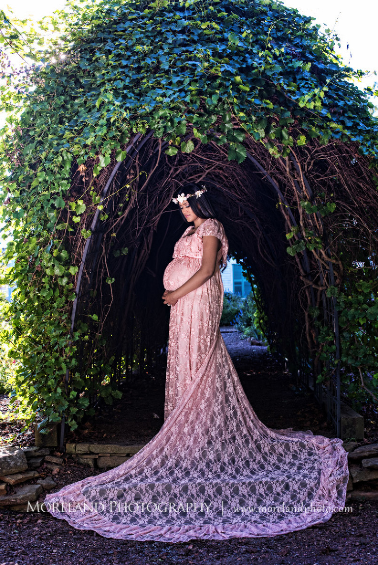 Pregnant Indian woman holding her stomach under a wooden archway, outdoor maternity, naturalistic maternity, beautiful, love, adoration, nature, natural, joy, romance, peaceful, protection, serene
