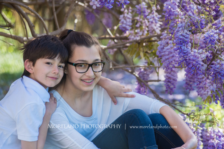 Portrait of a young brother with his arm around older sister shoulders smiling wearing white shirts sitting outside in the daytime in front of a purple flowry bush, Atlanta Portrait Photographer, Atlanta Child Photographer, Atlanta Family Photographer, Moreland Photography, Mike Moreland