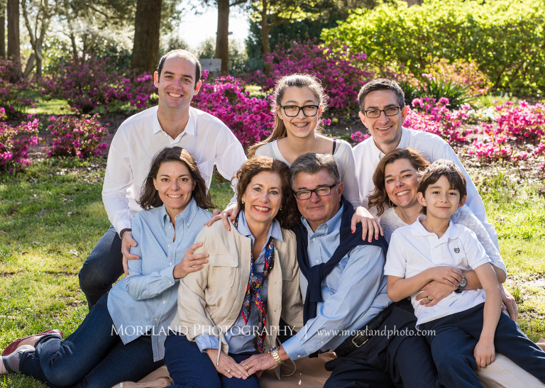 Portrait of smiling family of eight sitting together wearing navy white and beige outside during the daytime in front of pink floral bushes, Family Moreland Photography, Atlanta Portrait Photographer, Atlanta Child Photographer, Atlanta Family Photographer, Moreland Photography, Mike Moreland