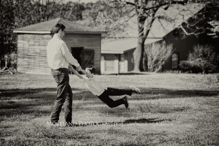 Black and white portarit of a father swinging his son around in front of a house outside during the daytime, Atlanta Portrait Photographer, Atlanta Child Photographer, Atlanta Family Photographer, Moreland Photography, Mike Moreland