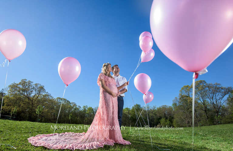 Pregnant wife and her husband stand next to each other as he touches her belly and she holds pink balloons, Atlanta Maternity Photographer, Maternity Photos Atlanta, Georgia Maternity Photography, Moreland Photography, Mike Moreland, Outdoor Maternity, Maternity on the River, 