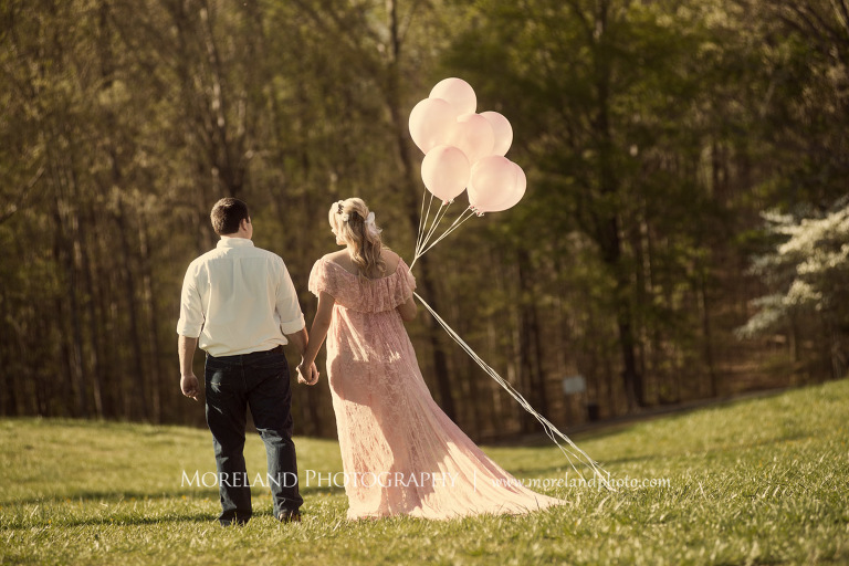 Husband and pregnant wife holds hands and the wife holds pink balloons as they walk across a field, Atlanta Maternity Photographer, Maternity Photos Atlanta, Georgia Maternity Photography, Moreland Photography, Mike Moreland, Outdoor Maternity, Maternity on the River, 