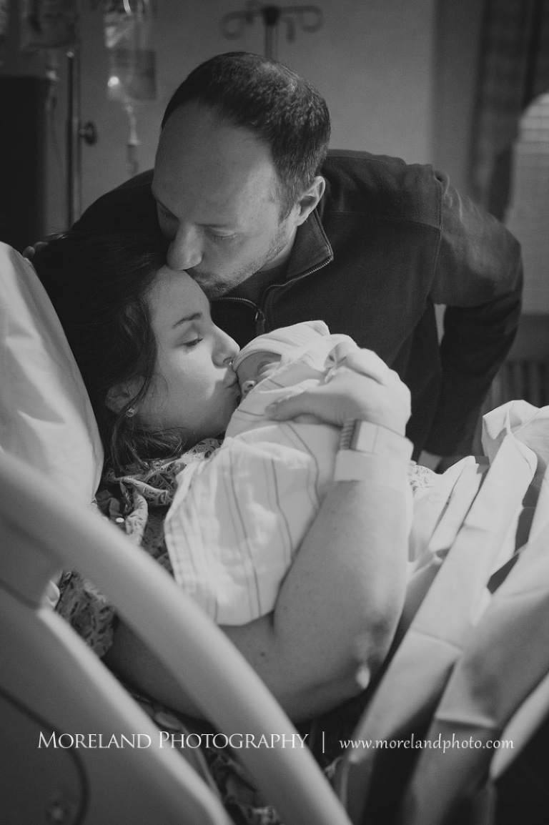Grey-scale image of a father kissing his wife's forehead as she kisses their newborn son, Atlanta Newborn Photography, Newborn Photographer Atlanta, Birth Photography, Natural Birth Photography, Hospital Photographer, Moreland Photography, Mike Moreland