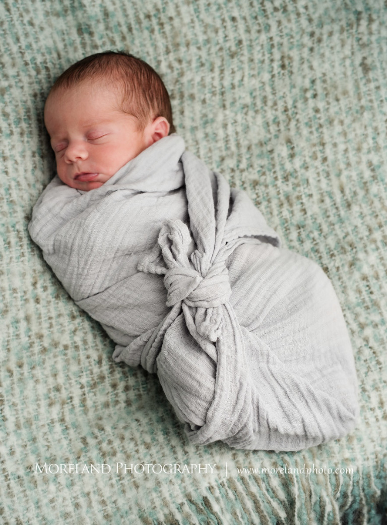A sleping newborn baby swaddled in a knotted blanket while on top of a green pillow, Atlanta Newborn Photography, Newborn Photographer Atlanta, Birth Photography, Natural Birth Photography, Hospital Photographer, Moreland Photography, Mike Moreland