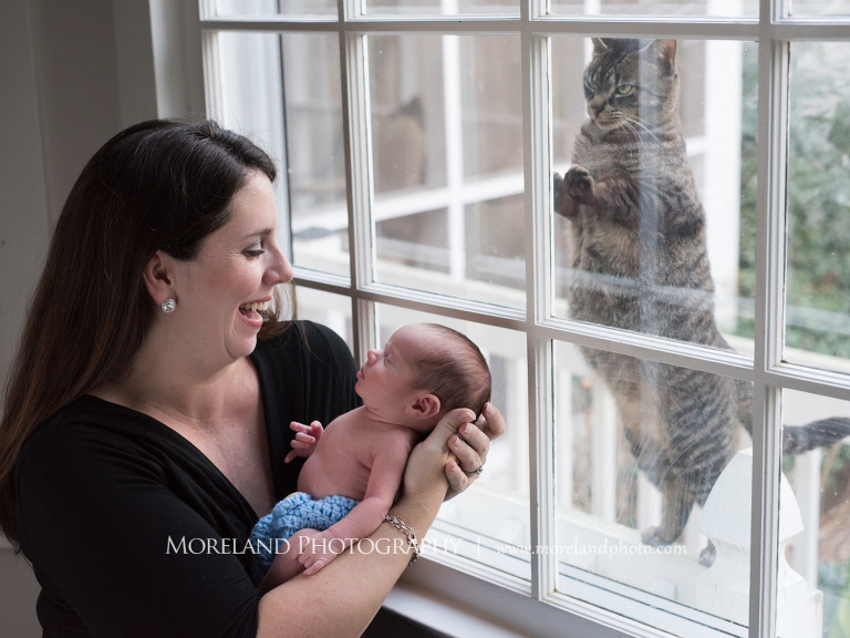 A laughing mother holding her sleeping newborn son while a cat paws at the window, Atlanta Newborn Photography, Newborn Photographer Atlanta, Birth Photography, Natural Birth Photography, Hospital Photographer, Moreland Photography, Mike Moreland