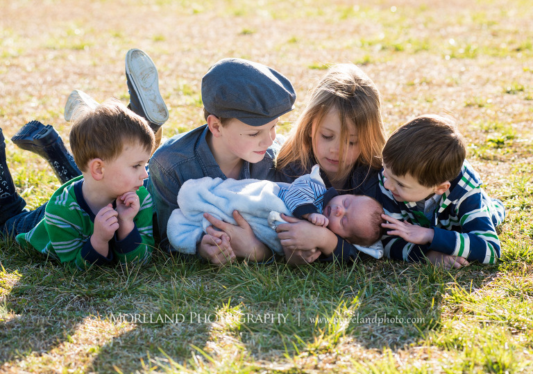 Medium close-up of four siblings laying in an open field of grass outside while holding their newborn baby brother, Family Newborn Photography, Atlanta Newborn Photography, Newborn Photographer Atlanta, Birth Photography, Natural Birth Photography, Hospital Photographer, Moreland Photography, Mike Moreland