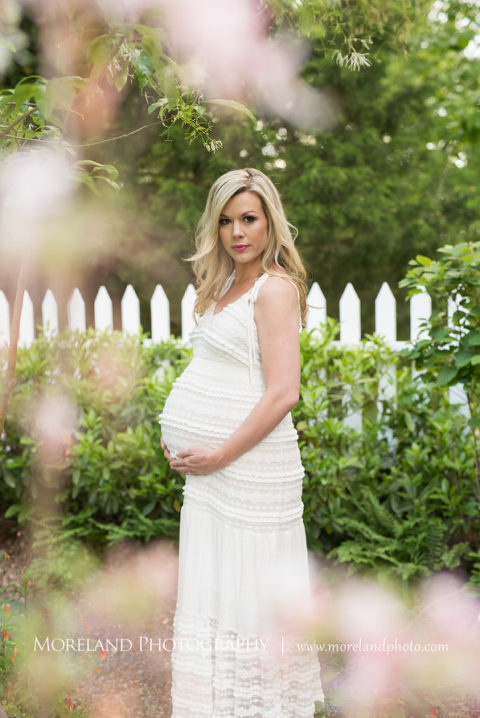 Portrait of pregnant woman standing outside in front of white fence during, the daytime holding her belly, Maternity Photography, Atlanta Maternity, Lifestyle Maternity Photography, Styled Maternity Shoot, Moreland Photography, Mike Moreland, Outdoor Maternity, Nature Maternity, 