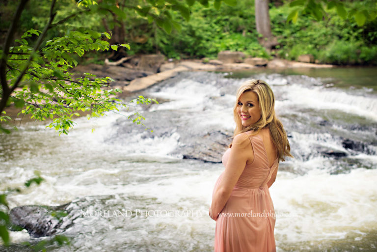 Portrait of pregnant woman holding her belly smiling looking over her shoulder standing in front of a river, Maternity Photography, Atlanta Maternity, Lifestyle Maternity Photography, Styled Maternity Shoot, Moreland Photography, Mike Moreland, Outdoor Maternity, Nature Maternity, 
