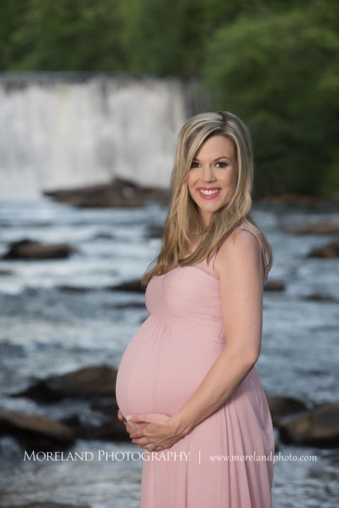 Portrait of pregnant woman in pink gown smiling holding her belly standing in front of a waterfall, Maternity Photography, Atlanta Maternity, Lifestyle Maternity Photography, Styled Maternity Shoot, Moreland Photography, Mike Moreland, Outdoor Maternity, Nature Maternity, 