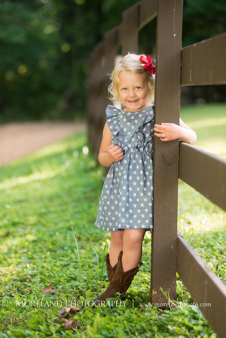 little girl smiling in polka dot dress by fence post, Mike Moreland, Moreland Photography, wedding photography, Atlanta wedding photography, detailed wedding photography, lifestyle wedding photography, Atlanta wedding photographer,