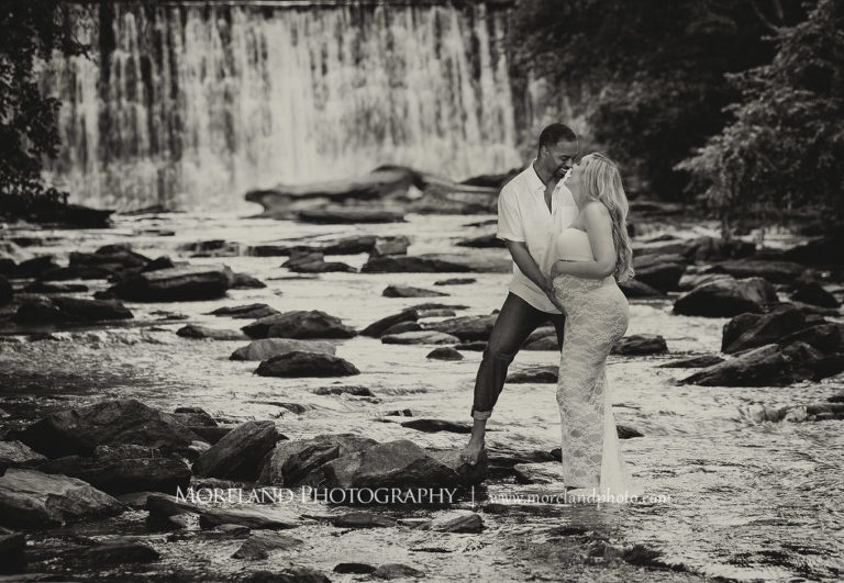 Black and white pregnant woman and husband standing in front of waterfall wearing white, lacey maternity dress, Mike Moreland, Moreland Photography, Atlanta Portrait Photographer, Maternity Photography Atlanta