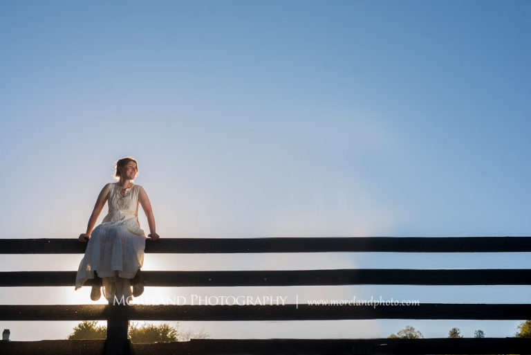 Georgia Senior portrait of a girl in nature sitting on a long black wooden fence , Mike Moreland, Moreland Photography, Atlanta Portrait Photographer, Senior Photography Atlanta, Kings Ridge Christian Academy, Nature, Equestrian, Georgia Senior Portrait, Outdoors Photography, Georgia Girl, Nature, Girl Sitting On Wood Fence, White Dress, Wooden Back Fence, , Stable 