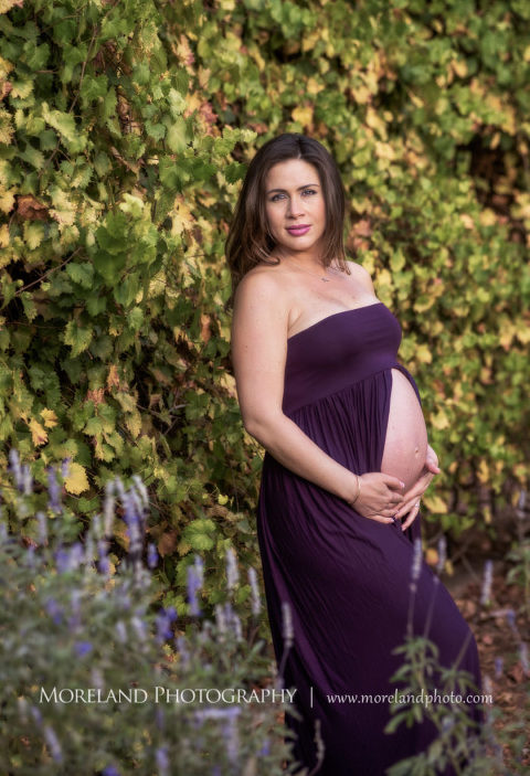 Pregnant mother smiling with her stomach exposed in a purple maternity dress under a green vine arch, Mike Moreland, Moreland Photography, Outdoor Photography, Atlanta Portrait Photographer, Maternity Photography Atlanta, New Born Photography, New Born Photography Atlanta, Baby, Downtown Atlanta, Family, Mother, Purple Maternity Dress