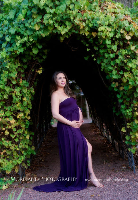 Pregnant mother smiling with her stomach exposed in a purple maternity dress under a green vine arch, Mike Moreland, Moreland Photography, Outdoor Photography, Atlanta Portrait Photographer, Maternity Photography Atlanta, New Born Photography, New Born Photography Atlanta, Baby, Downtown Atlanta, Family, Mother, Purple Maternity Dress