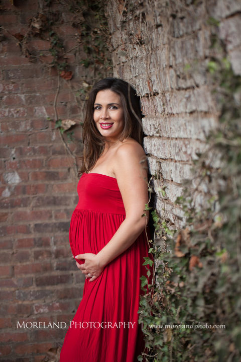 Mother holding her swollen belly wearing a red dress, Mike Moreland, Moreland Photography, Atlanta Portrait Photographer, Maternity Photography Atlanta, New Born Photography, New Born Photography Atlanta, Baby, Downtown Atlanta, Family, Mother, Red Maternity Dress, Brick Wall, 
