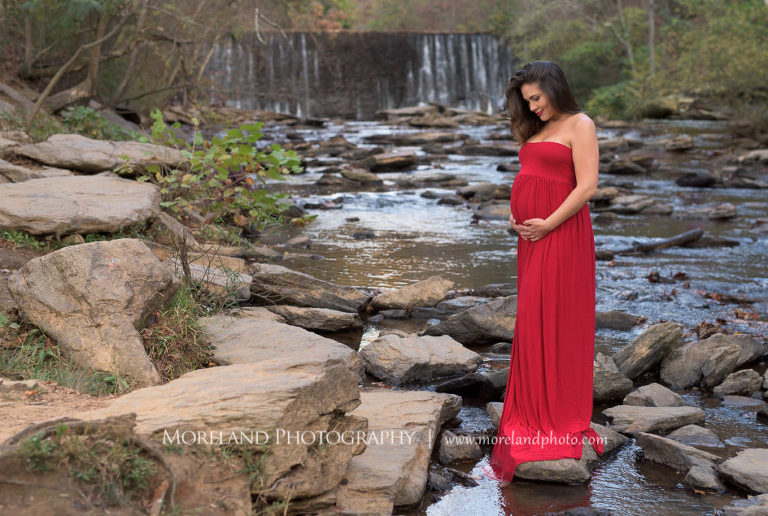 Maternity shoot of mother holding her belly wearing a red dress with waterfall in the background, Mike Moreland, Moreland Photography, Atlanta Portrait Photographer, Maternity Photography Atlanta, New Born Photography, New Born Photography Atlanta, Baby, Downtown Atlanta, Family, Mother, River Stream, Waterfall, Red Maternity Dress, Outdoors Photoshoot