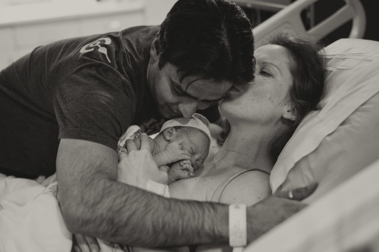 Mother kissing father as he hugs his family, The Kahn's birth shoot, Piedmont Hospital Birth Shoot, Mike Moreland, Moreland Photography, Birth Photography, Atlanta Portrait Photographer, Photography Atlanta, New Born Photography, New Born Photography Atlanta, Baby, Family, Mother, Father, Little Moment Photography, Black and white photography, Baby Boy