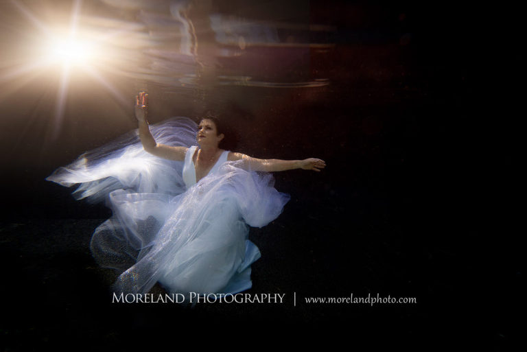 woman in white dress underwater reaching toward the surface with sunflare, underwater portraits, portrait photography atlanta, moreland photography, florida underwater portraits, underwater photography, nikon, atlanta underwater photographer