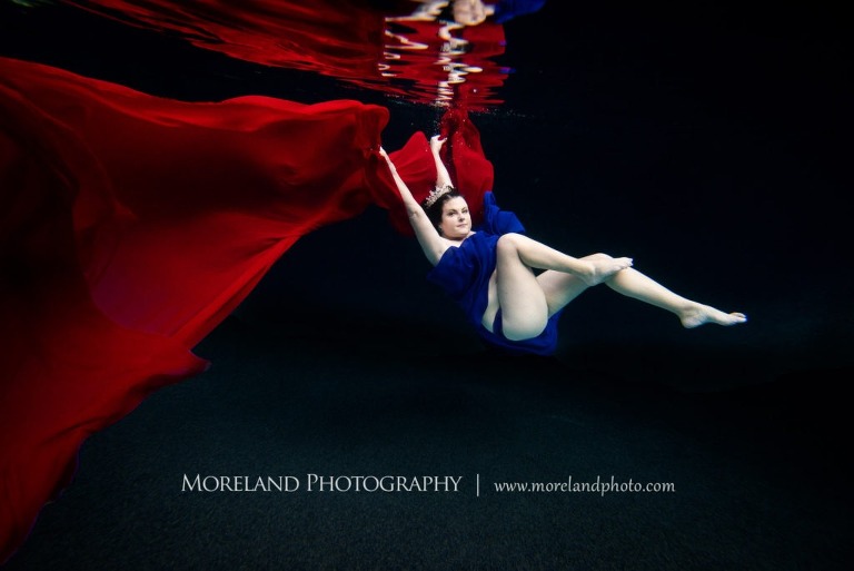 woman posing for underwater photo shoot in blue and red dress reaching for the surface, underwater portraits, creative photography atlanta, creative edge workshops, moreland photography, florida underwater portraits, underwater photography, nikon, underwater pictures, majestic underwater portraits